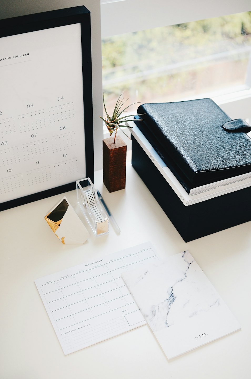 Brightly lit desk with calendar, air plant, and planner.